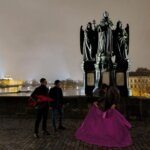 Tres personas interactuando frente a una escultura en Praga de noche