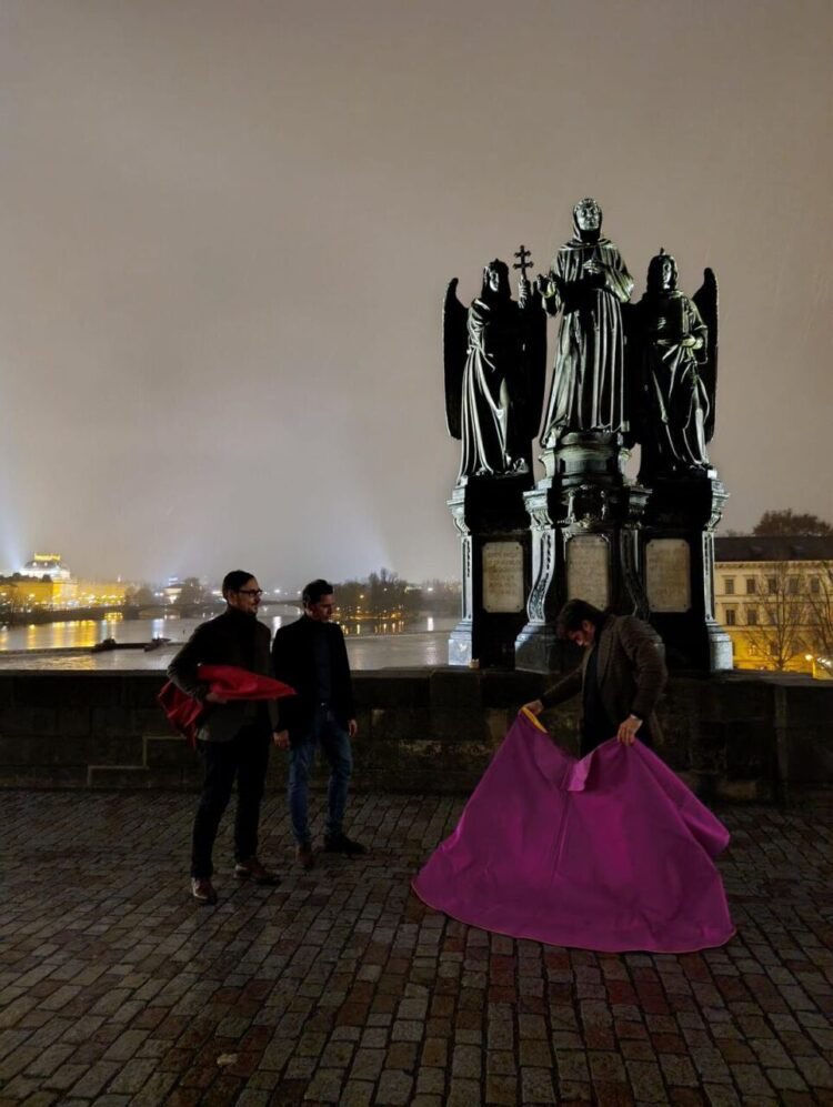 Tres personas interactuando frente a una escultura en Praga de noche