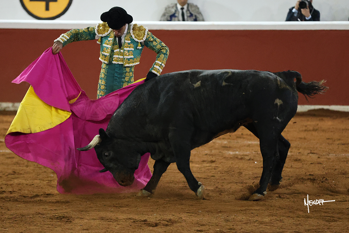 Un torero con un capote de colores en la plaza de toros.