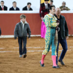 Torero sonriente caminando con dos niños en la plaza de toros.