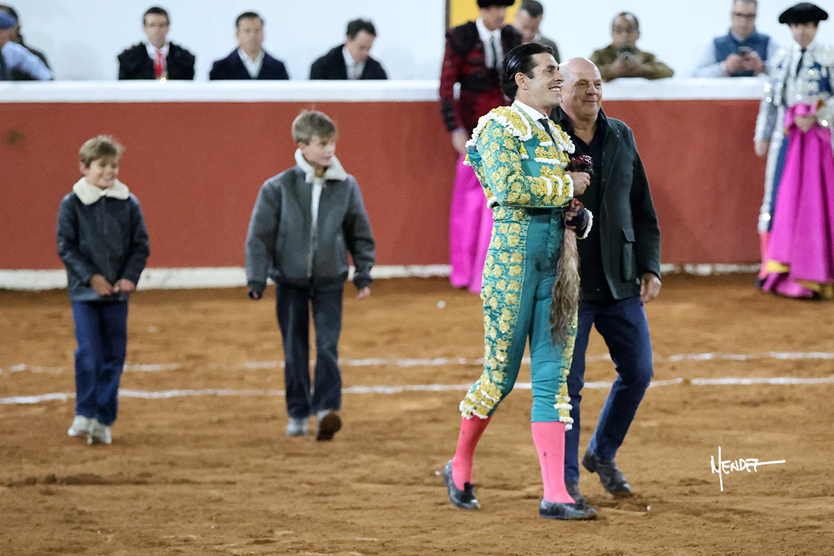 Torero sonriente caminando con dos niños en la plaza de toros.