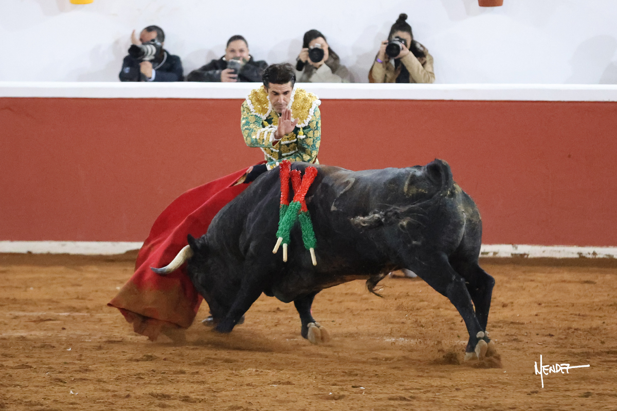 Torero vestido de luces lidiando un toro en la plaza de toros.